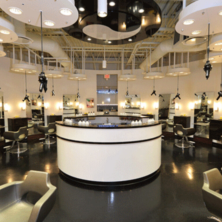 Modern hair salon interior with a central circular reception desk, styling stations with mirrors, and hanging hair dryers under bright ceiling lights. - Jón Alan Salon in Nashville and Franklin, TN